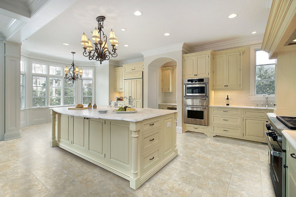 Inspiration for a large transitional l-shaped ceramic tile and gray floor open concept kitchen remodel with a farmhouse sink, raised-panel cabinets, beige cabinets, marble countertops, white backsplash, subway tile backsplash, stainless steel appliances and an island
