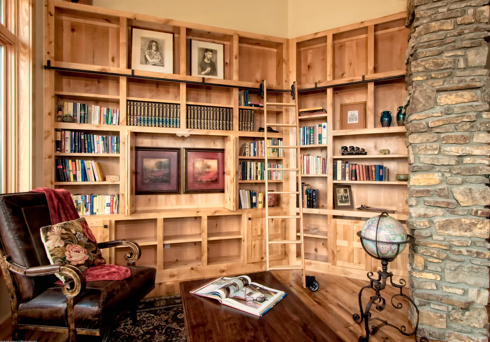 This is an example of a mid-sized country home office in Denver with a library, beige walls, medium hardwood floors, a standard fireplace, a stone fireplace surround and brown floor.