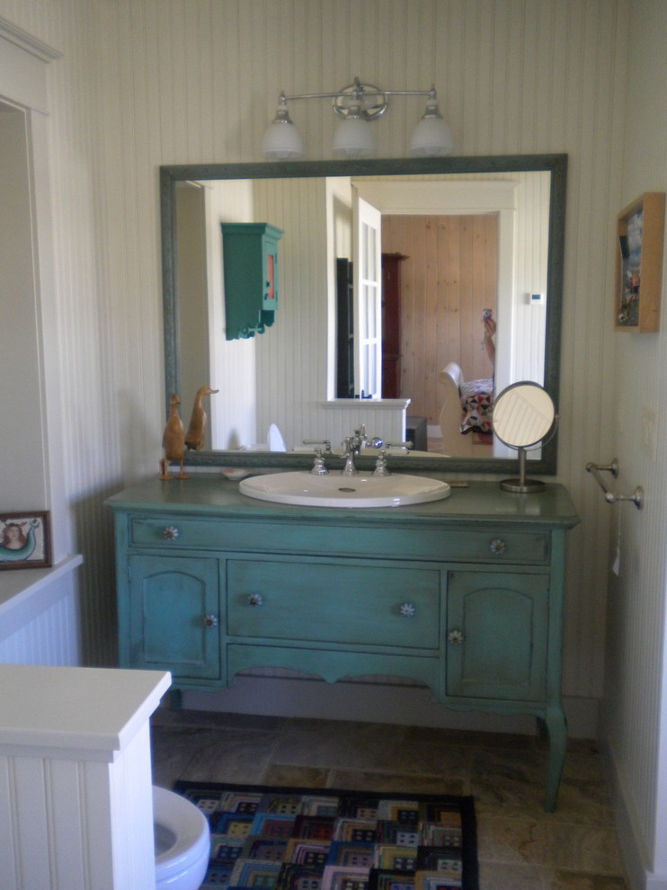 Photo of a mid-sized country 3/4 bathroom in Other with recessed-panel cabinets, turquoise cabinets, a one-piece toilet, white walls, slate floors, a drop-in sink, wood benchtops and turquoise benchtops.