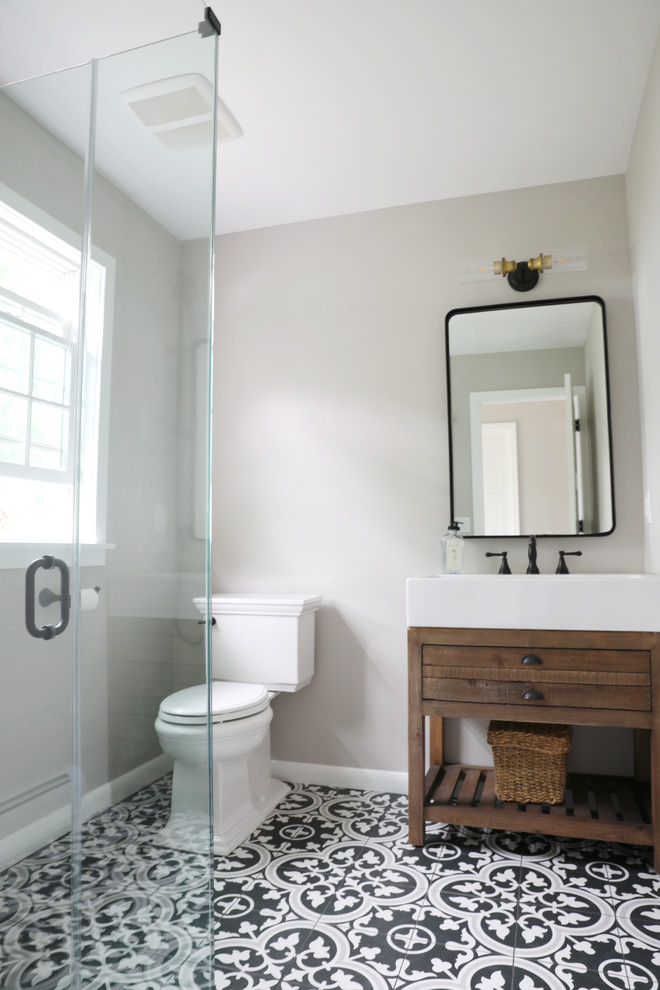 Photo of a mid-sized country 3/4 bathroom in New York with dark wood cabinets, black and white tile, grey walls, cement tiles, white benchtops, furniture-like cabinets, an open shower, a two-piece toilet, an integrated sink, multi-coloured floor and a hinged shower door.