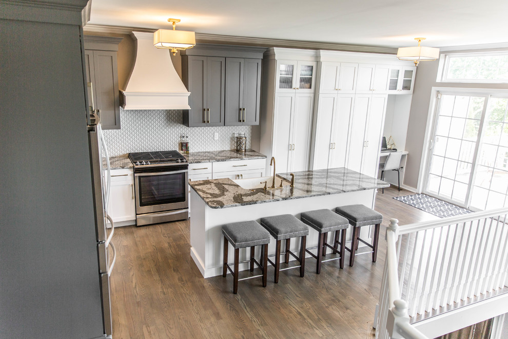 Mid-sized transitional l-shaped medium tone wood floor eat-in kitchen photo in Philadelphia with a farmhouse sink, shaker cabinets, white cabinets, quartz countertops, gray backsplash, porcelain backsplash, stainless steel appliances and an island