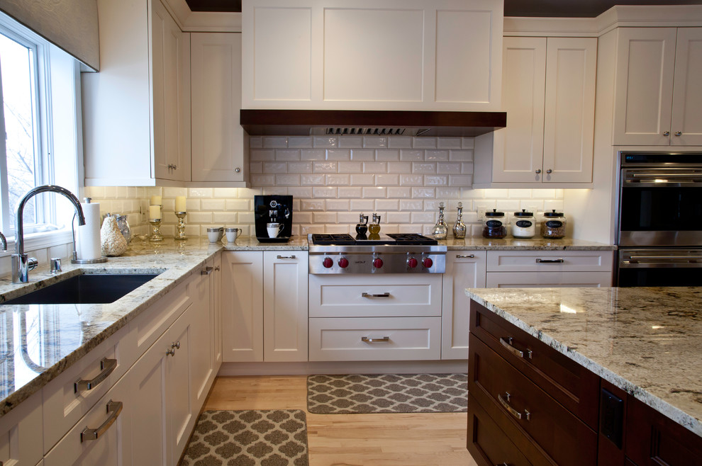 Open concept kitchen - large transitional l-shaped light wood floor and brown floor open concept kitchen idea with an undermount sink, shaker cabinets, white cabinets, granite countertops, white backsplash, subway tile backsplash, paneled appliances and an island