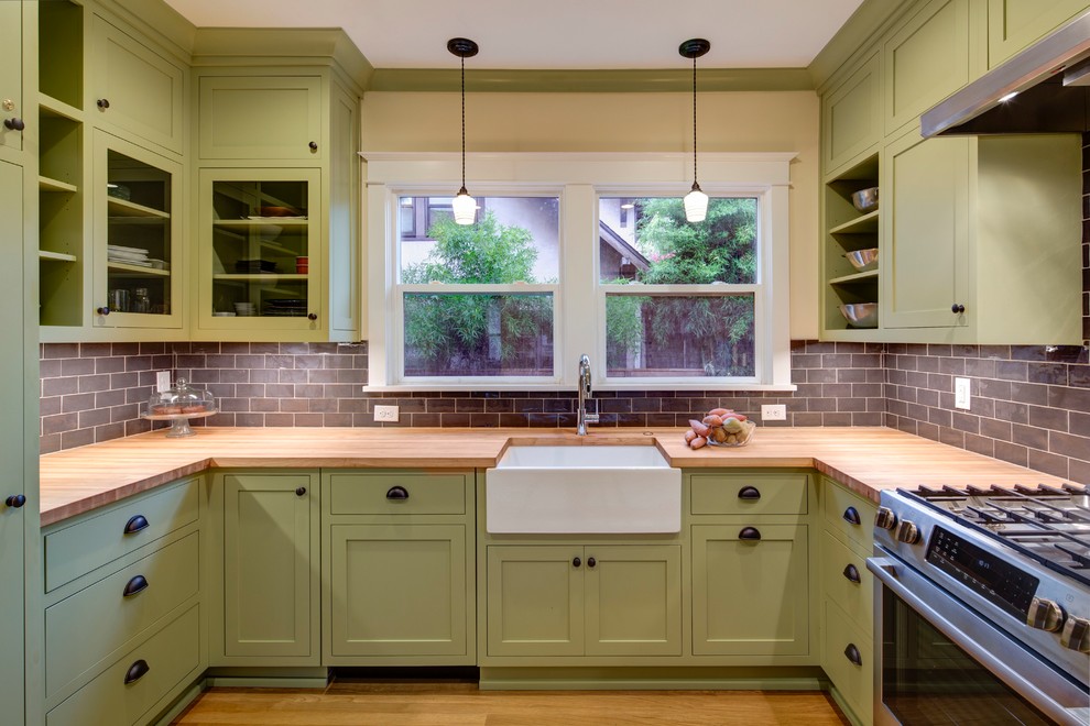 This is an example of a mid-sized arts and crafts u-shaped separate kitchen in Portland with a farmhouse sink, shaker cabinets, green cabinets, wood benchtops, blue splashback, ceramic splashback, stainless steel appliances, light hardwood floors and no island.
