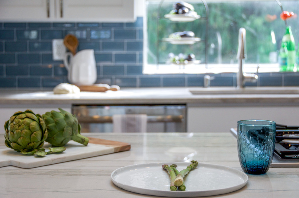 Example of a large transitional galley medium tone wood floor and brown floor open concept kitchen design in Seattle with an undermount sink, shaker cabinets, white cabinets, quartz countertops, blue backsplash, subway tile backsplash, stainless steel appliances, an island and multicolored countertops