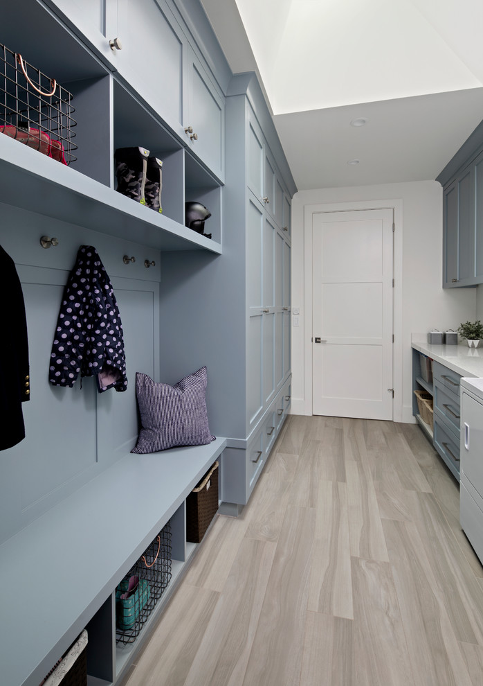 Inspiration for a large country galley utility room in San Francisco with a drop-in sink, shaker cabinets, blue cabinets, solid surface benchtops, white walls, medium hardwood floors, a side-by-side washer and dryer, grey floor and white benchtop.