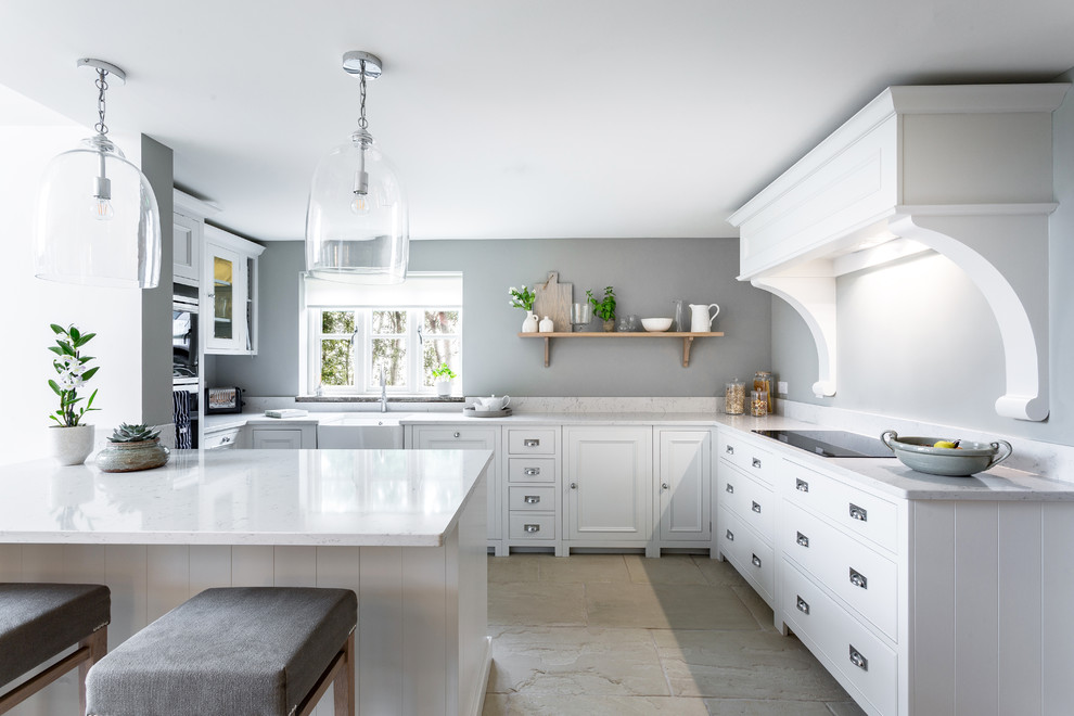 This is an example of a mid-sized country u-shaped open plan kitchen in Other with a farmhouse sink, beaded inset cabinets, solid surface benchtops, black appliances, limestone floors, a peninsula, beige floor, white benchtop and white cabinets.