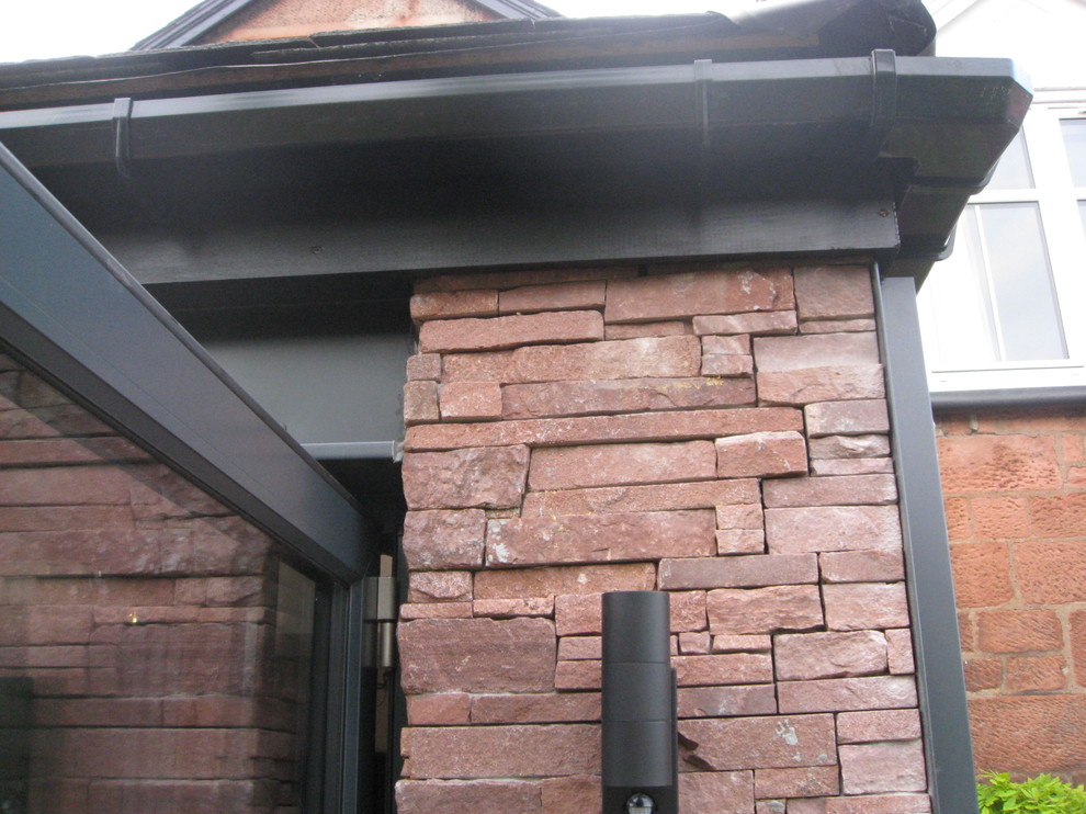 This is an example of a mid-sized contemporary one-storey red townhouse exterior in Glasgow with stone veneer, a gable roof and a tile roof.