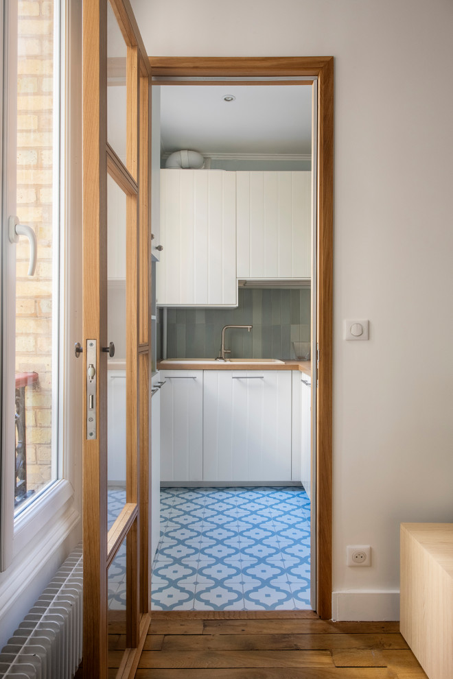 This is an example of a mid-sized mediterranean l-shaped separate kitchen in Paris with a single-bowl sink, flat-panel cabinets, white cabinets, wood benchtops, blue splashback, ceramic splashback, stainless steel appliances, cement tiles, no island, blue floor and beige benchtop.