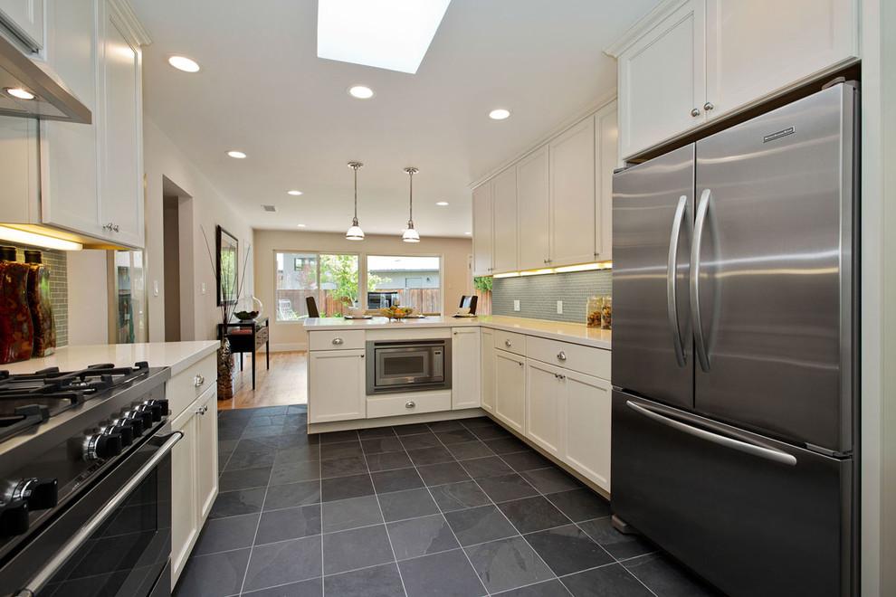 Photo of a large contemporary l-shaped eat-in kitchen in San Francisco with an undermount sink, recessed-panel cabinets, white cabinets, solid surface benchtops, grey splashback, ceramic splashback, stainless steel appliances, slate floors and no island.