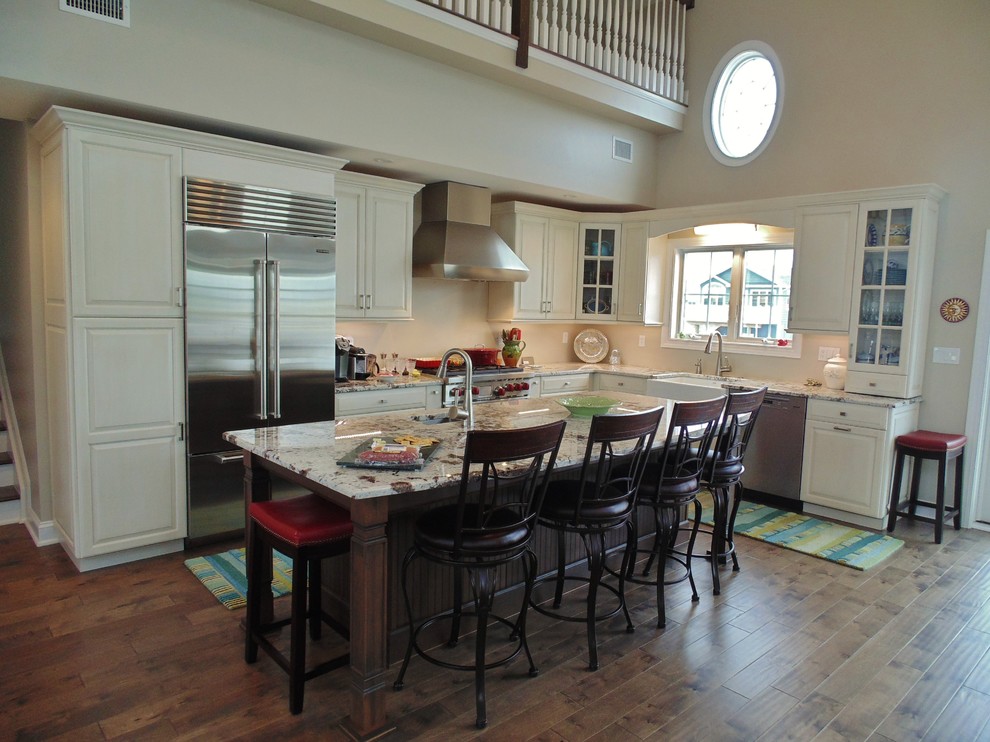Mid-sized transitional l-shaped medium tone wood floor eat-in kitchen photo in New York with a farmhouse sink, raised-panel cabinets, white cabinets, granite countertops, beige backsplash, stainless steel appliances and an island