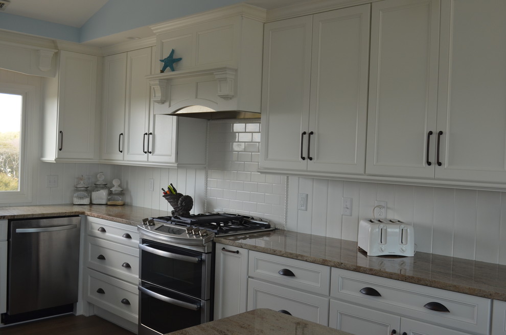 Photo of a large beach style u-shaped eat-in kitchen in Other with an undermount sink, recessed-panel cabinets, white cabinets, granite benchtops, white splashback, timber splashback, stainless steel appliances, medium hardwood floors, with island, brown floor and brown benchtop.