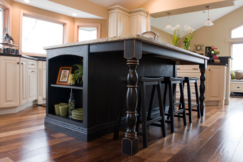 Example of a large transitional l-shaped medium tone wood floor eat-in kitchen design with an undermount sink, raised-panel cabinets, distressed cabinets, granite countertops, black backsplash, stainless steel appliances and an island
