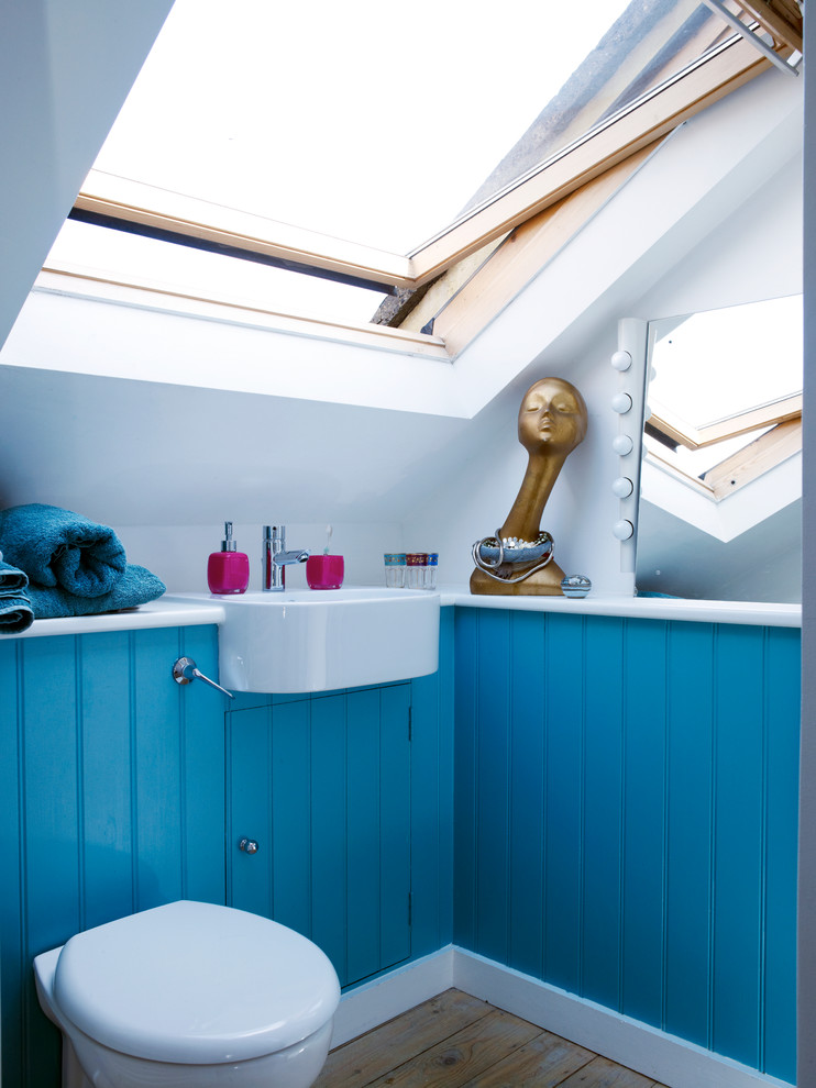 Photo of a small contemporary bathroom in London with a wall-mount sink, blue cabinets, a wall-mount toilet, white walls and medium hardwood floors.