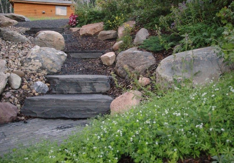 Small country sloped partial sun formal garden in Calgary with a garden path and natural stone pavers.