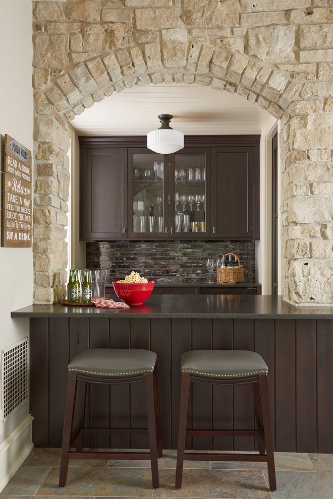 This is an example of a small traditional seated home bar in Minneapolis with recessed-panel cabinets, dark wood cabinets, multi-coloured splashback, mosaic tile splashback, ceramic floors and multi-coloured floor.