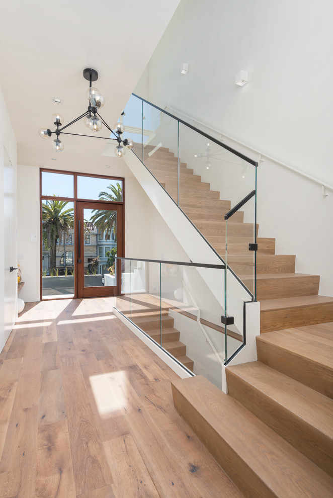 Photo of a mid-sized contemporary front door in San Francisco with white walls, light hardwood floors, a pivot front door, a glass front door and beige floor.
