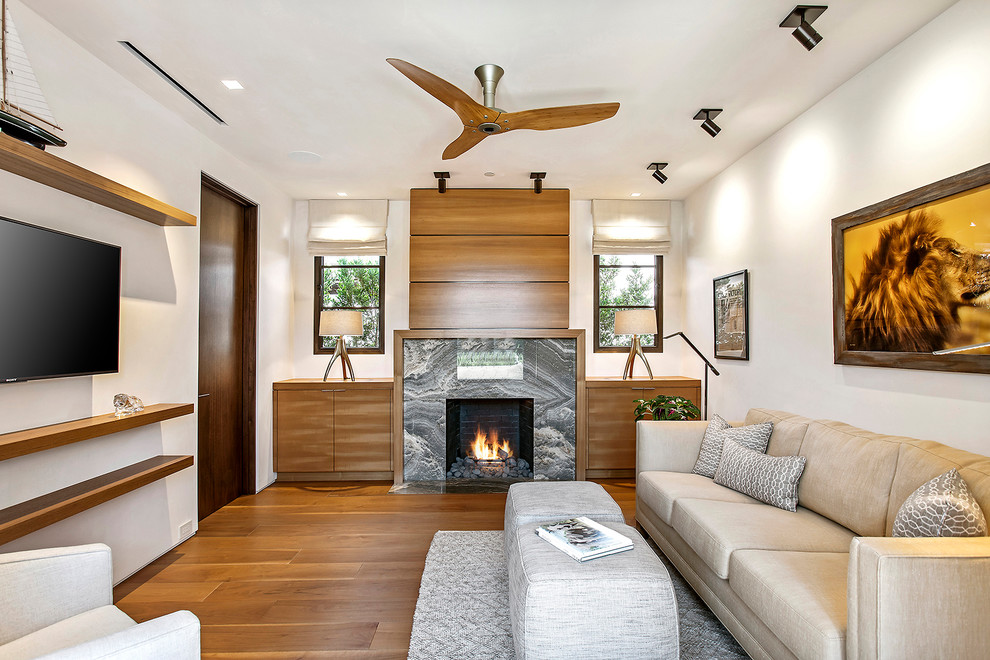 Design ideas for a mid-sized contemporary enclosed family room in Los Angeles with white walls, medium hardwood floors, a standard fireplace, a wall-mounted tv, a stone fireplace surround and brown floor.