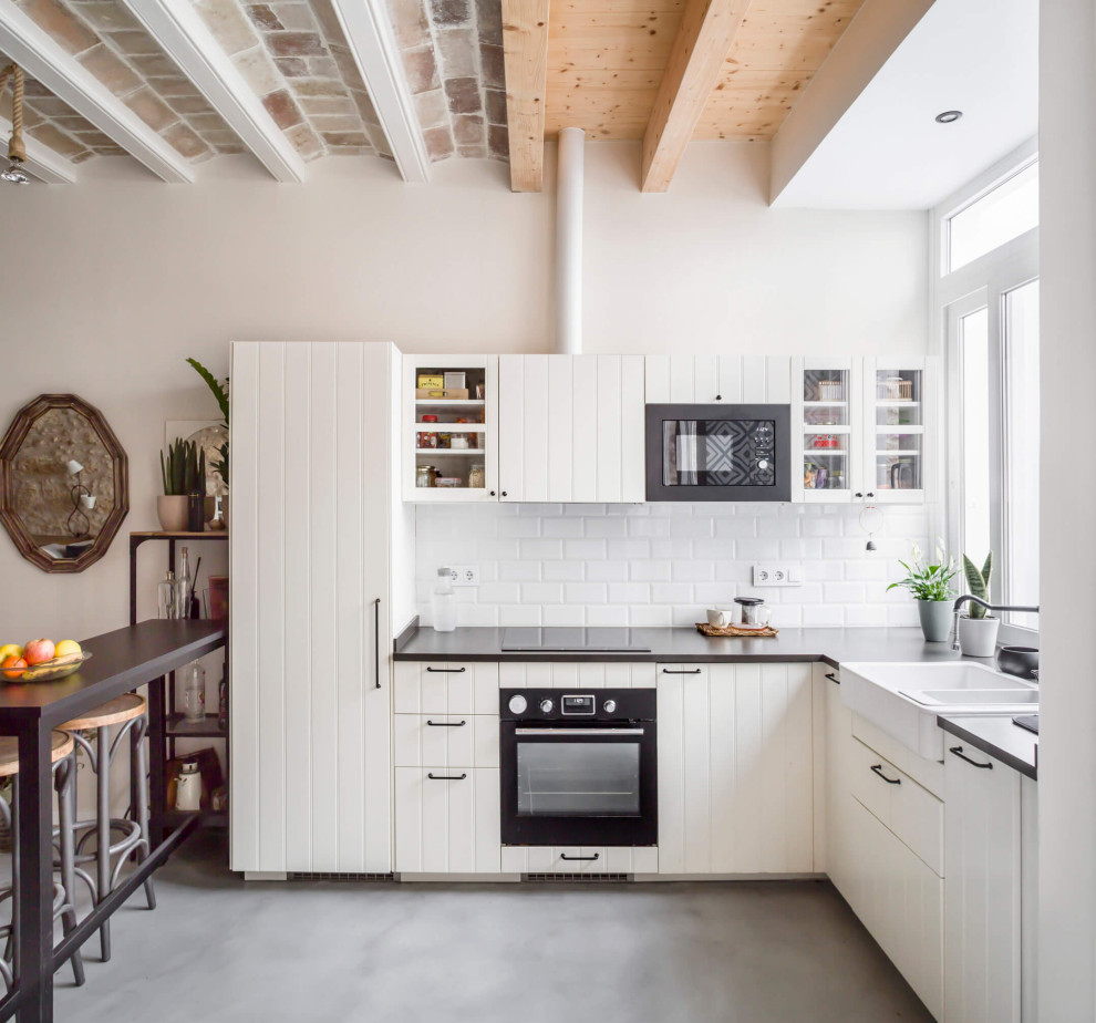 Small coastal l-shaped open plan kitchen in Other with a double-bowl sink, raised-panel cabinets, white cabinets, engineered stone countertops, white splashback, ceramic splashback, black appliances, concrete flooring, no island, grey floors, black worktops and exposed beams.