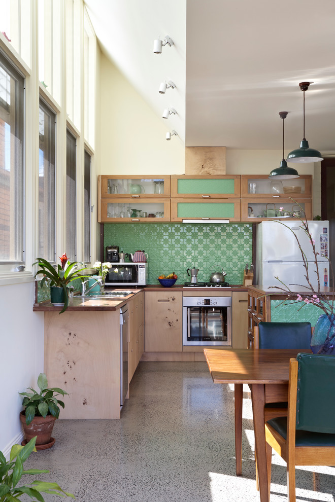 Inspiration for a mid-sized contemporary l-shaped eat-in kitchen in Melbourne with glass-front cabinets, medium wood cabinets, wood benchtops, green splashback, white appliances, concrete floors, with island, a single-bowl sink, metal splashback, grey floor and brown benchtop.