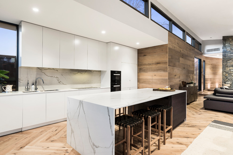 Modern single-wall eat-in kitchen in Melbourne with an undermount sink, flat-panel cabinets, white cabinets, quartz benchtops, multi-coloured splashback, stone slab splashback, black appliances, light hardwood floors, with island and brown floor.