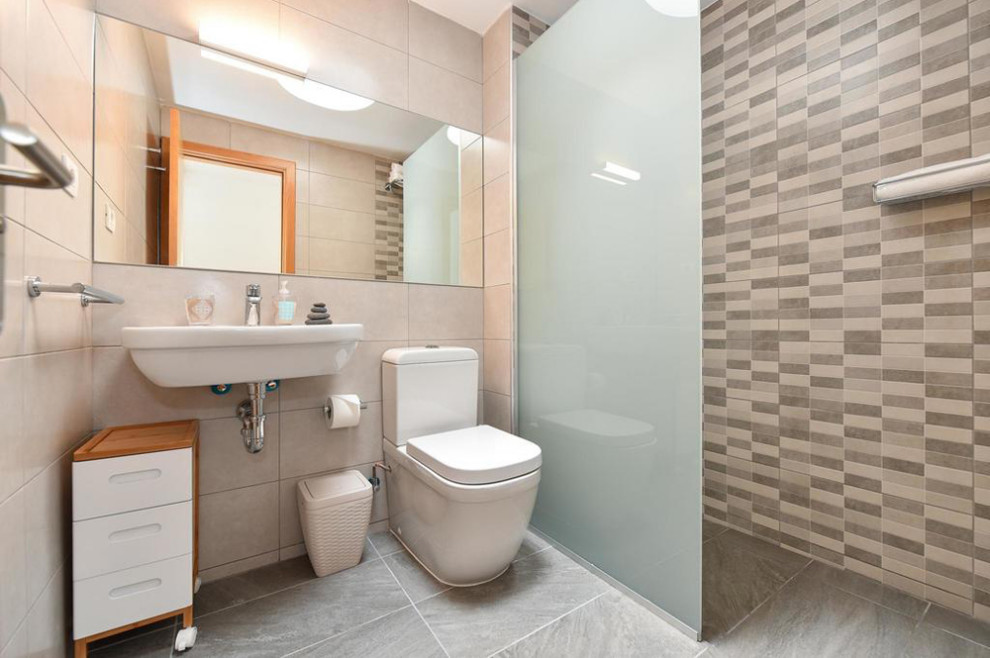 This is an example of a mid-sized mediterranean powder room in Other with white cabinets, a one-piece toilet, beige tile, ceramic tile, white walls, a trough sink, brown floor and a floating vanity.