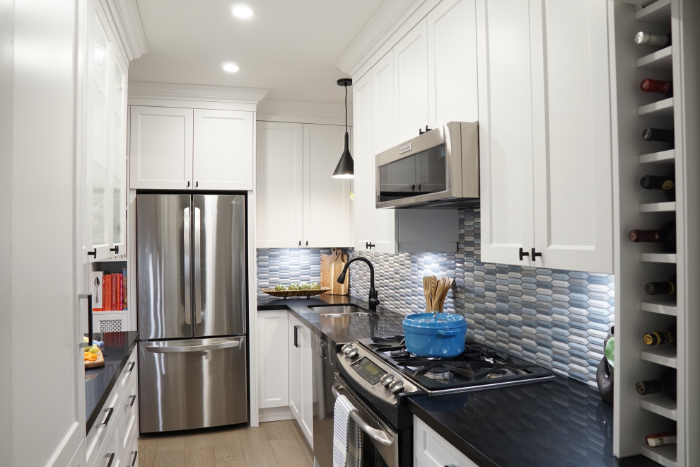 Kitchen - mid-sized transitional galley light wood floor and gray floor kitchen idea in Toronto with an undermount sink, glass-front cabinets, white cabinets, quartz countertops, blue backsplash, ceramic backsplash, stainless steel appliances and black countertops