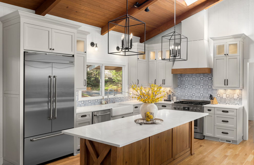 Design ideas for a country l-shaped kitchen in Portland with a farmhouse sink, shaker cabinets, grey cabinets, grey splashback, stainless steel appliances, light hardwood floors, with island, beige floor and white benchtop.