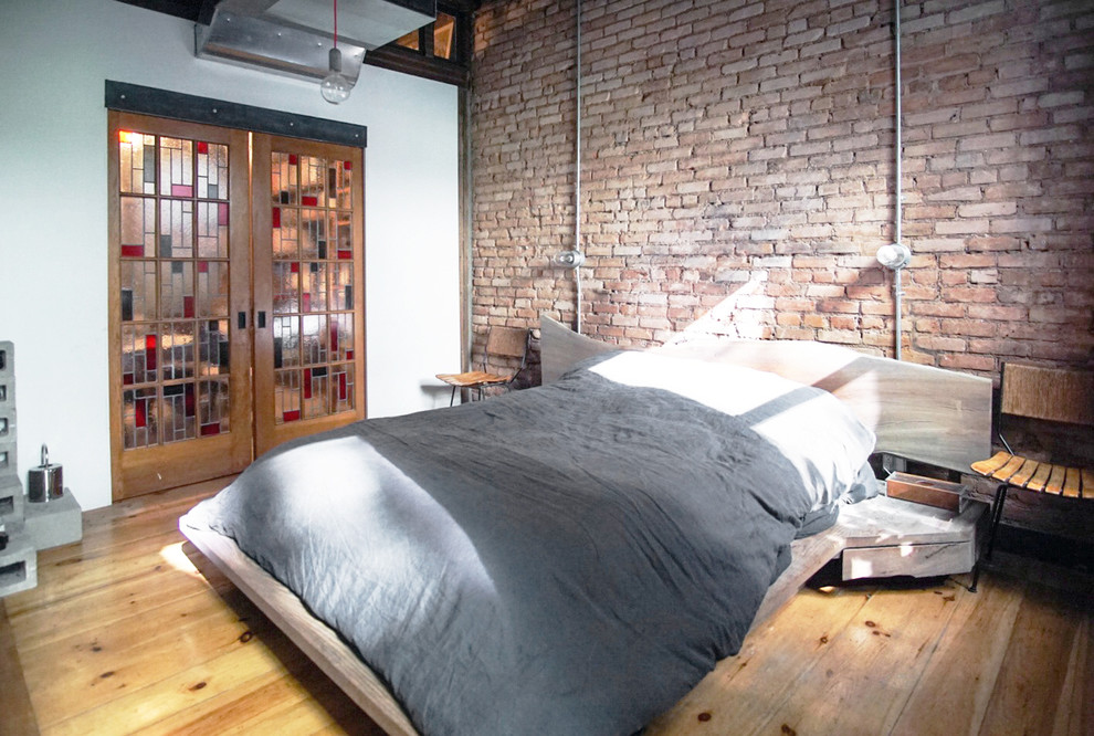 Photo of a mid-sized industrial master bedroom in New York with white walls and light hardwood floors.