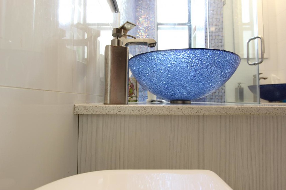 Photo of a small contemporary 3/4 bathroom in New York with a vessel sink, flat-panel cabinets, white cabinets, engineered quartz benchtops, a corner shower, blue tile, mosaic tile, white walls, a one-piece toilet and ceramic floors.