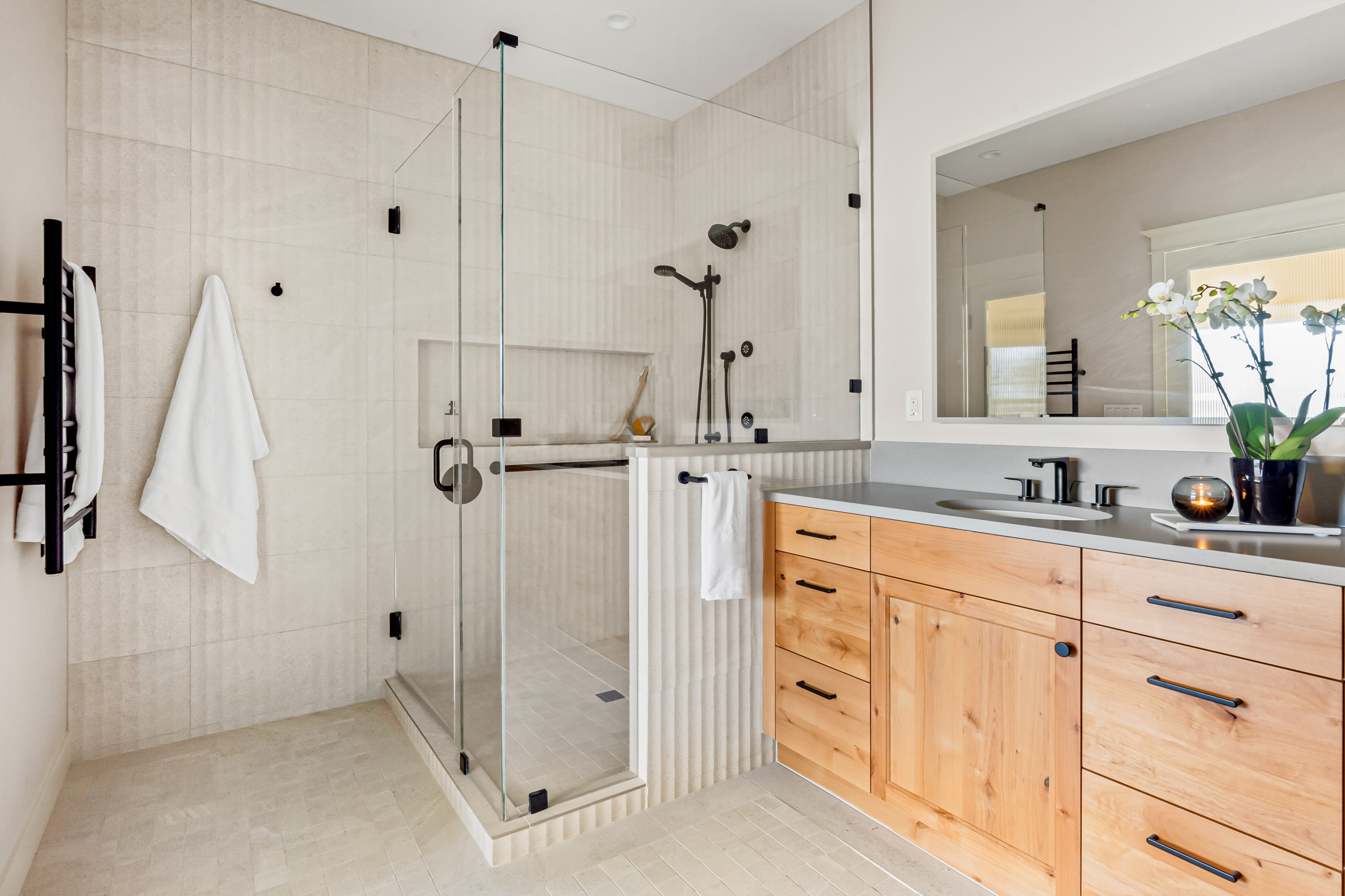 A bright, warm contemporary bathroom with a curbless walk-in shower, frameless glass enclosure, a built-in bench, and a sleek horizontal grab bar mounted on the tile wall.