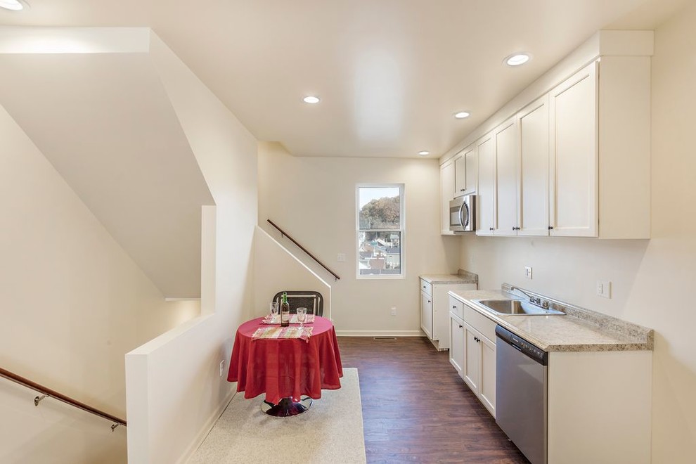 Small transitional galley brown floor eat-in kitchen photo with a single-bowl sink, shaker cabinets, white cabinets, laminate countertops, beige backsplash, stainless steel appliances and no island