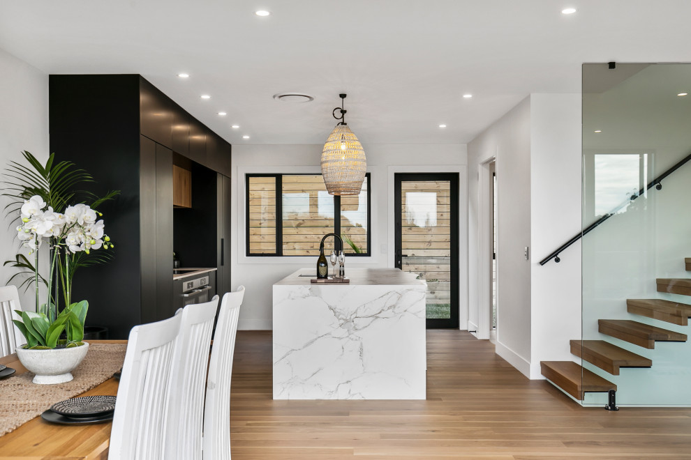 Photo of a mid-sized contemporary galley eat-in kitchen in Auckland with an undermount sink, black cabinets, tile benchtops, white splashback, stone tile splashback, stainless steel appliances, medium hardwood floors, with island and white benchtop.