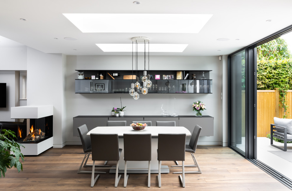 Inspiration for an expansive contemporary open plan dining in Surrey with white walls, medium hardwood floors, a two-sided fireplace, a plaster fireplace surround and brown floor.