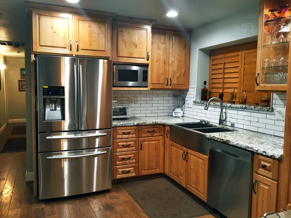 Example of a mid-sized mountain style u-shaped dark wood floor and brown floor enclosed kitchen design with a peninsula, a farmhouse sink, raised-panel cabinets, dark wood cabinets, quartz countertops, white backsplash, subway tile backsplash and stainless steel appliances