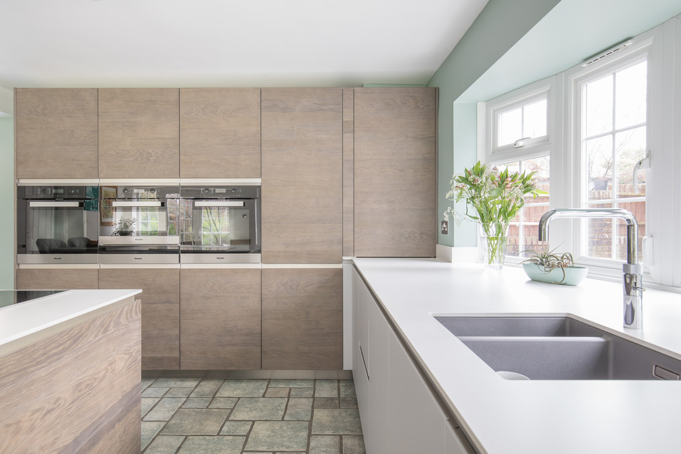 Inspiration for a mid-sized contemporary u-shaped kitchen in Sussex with an integrated sink, flat-panel cabinets, medium wood cabinets, solid surface benchtops, panelled appliances and with island.