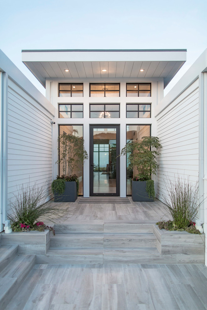 This is an example of a beach style front door in Los Angeles with white walls, light hardwood floors, a single front door, a glass front door and beige floor.