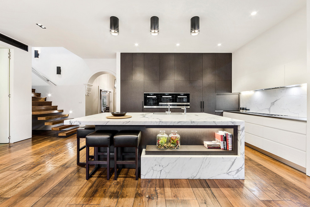 This is an example of a large contemporary l-shaped eat-in kitchen in Melbourne with an undermount sink, flat-panel cabinets, white cabinets, marble benchtops, stone slab splashback and with island.
