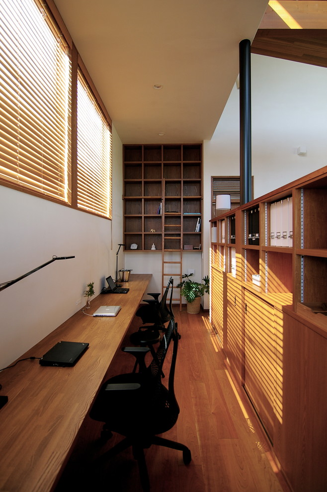 Photo of a midcentury study room in Other with white walls, medium hardwood floors, no fireplace, a built-in desk and brown floor.