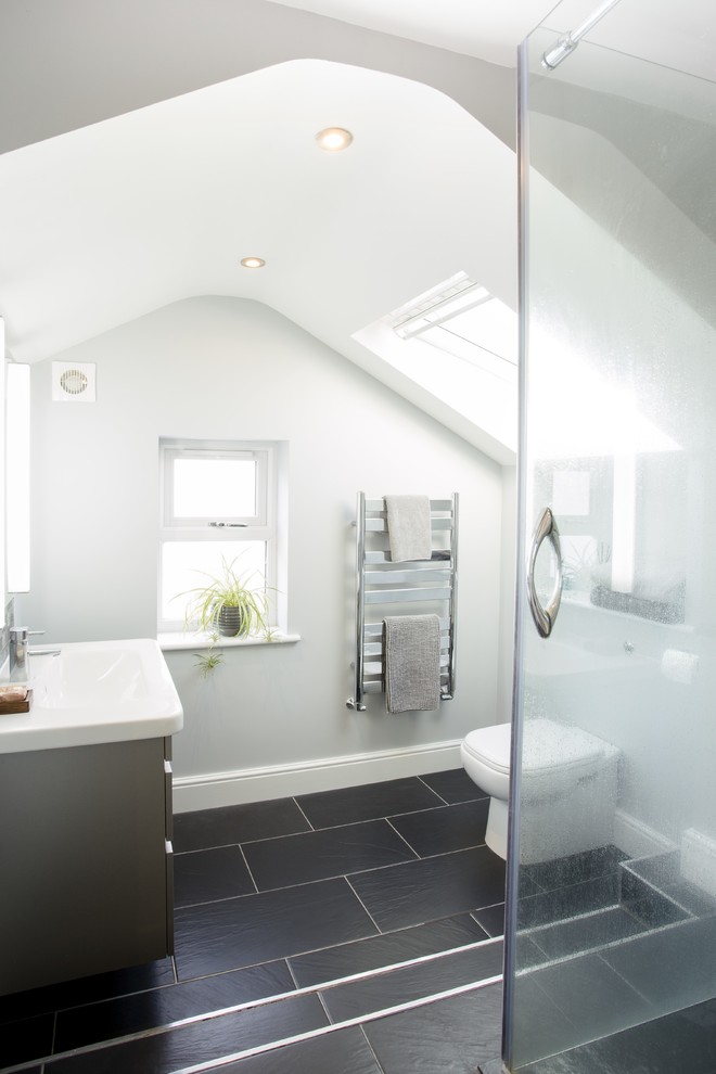 This is an example of a mid-sized contemporary master bathroom in Surrey with flat-panel cabinets, grey cabinets, an open shower, a one-piece toilet, white walls, ceramic floors, a console sink, solid surface benchtops, black floor and a hinged shower door.