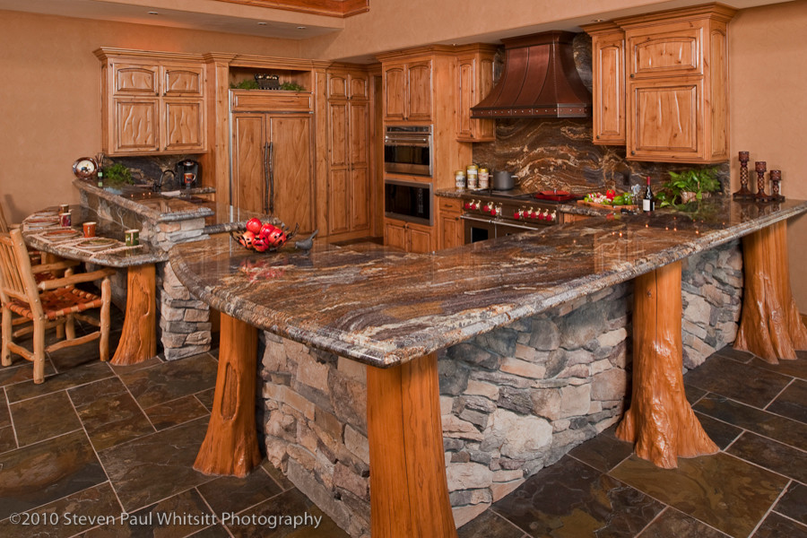 Example of a huge mountain style u-shaped slate floor open concept kitchen design with an undermount sink, raised-panel cabinets, distressed cabinets, granite countertops, multicolored backsplash, stone slab backsplash, stainless steel appliances and a peninsula