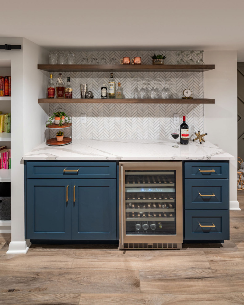 This is an example of a small transitional single-wall home bar in Columbus with recessed-panel cabinets, blue cabinets, quartz benchtops, white splashback, mosaic tile splashback, vinyl floors, grey floor and white benchtop.