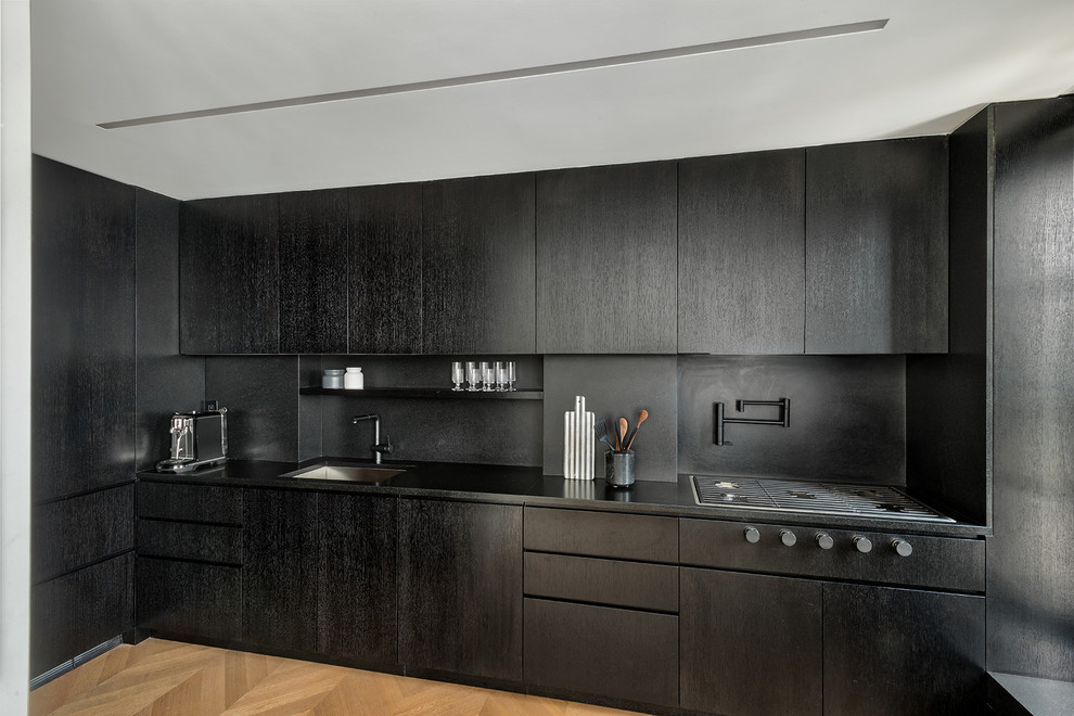 This is an example of a small contemporary kitchen in New York with an undermount sink, black cabinets, granite benchtops, black splashback, black appliances, medium hardwood floors, brown floor, black benchtop and flat-panel cabinets.