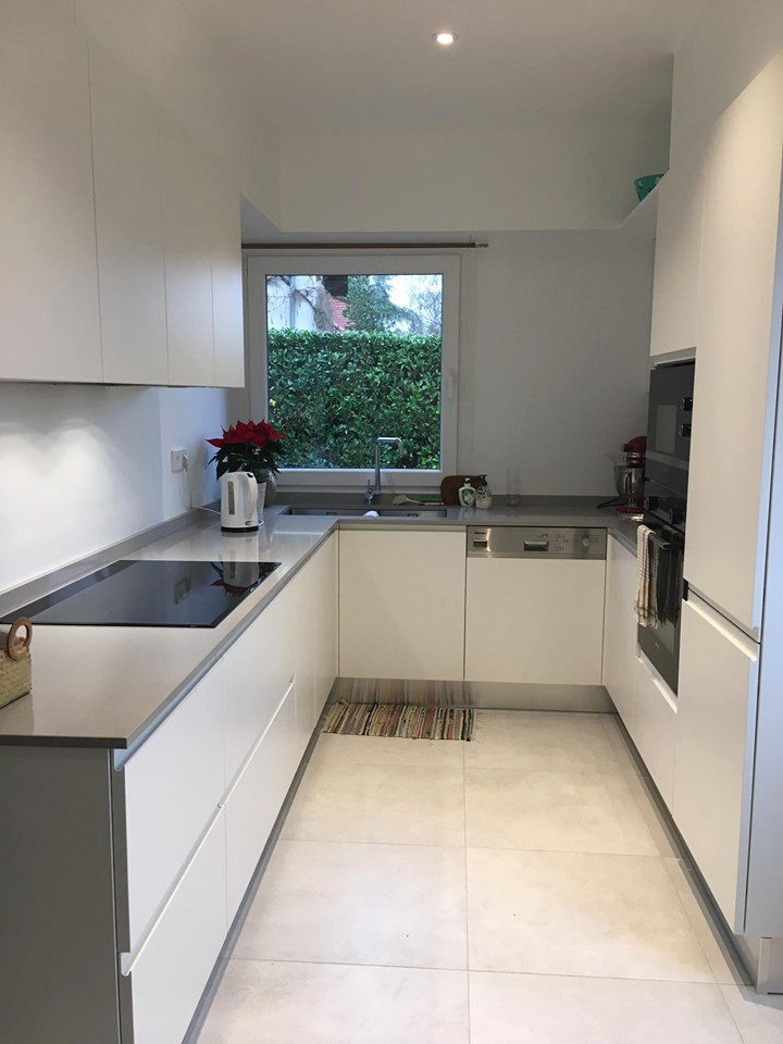 Photo of a small modern u-shaped separate kitchen in Other with a double-bowl sink, flat-panel cabinets, white cabinets, zinc benchtops, beige splashback, glass sheet splashback, stainless steel appliances, porcelain floors, no island, multi-coloured floor, grey benchtop and coffered.