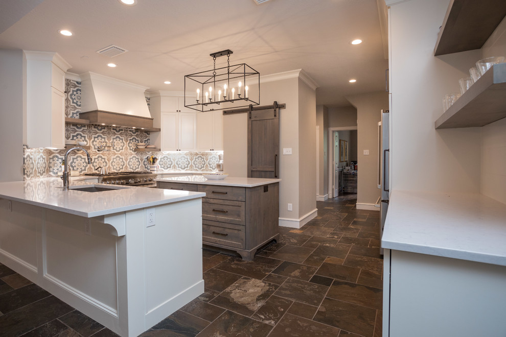 This is an example of a large country u-shaped kitchen pantry in Houston with an undermount sink, shaker cabinets, white cabinets, quartz benchtops, multi-coloured splashback, mosaic tile splashback, stainless steel appliances, cement tiles, with island, white benchtop and vaulted.