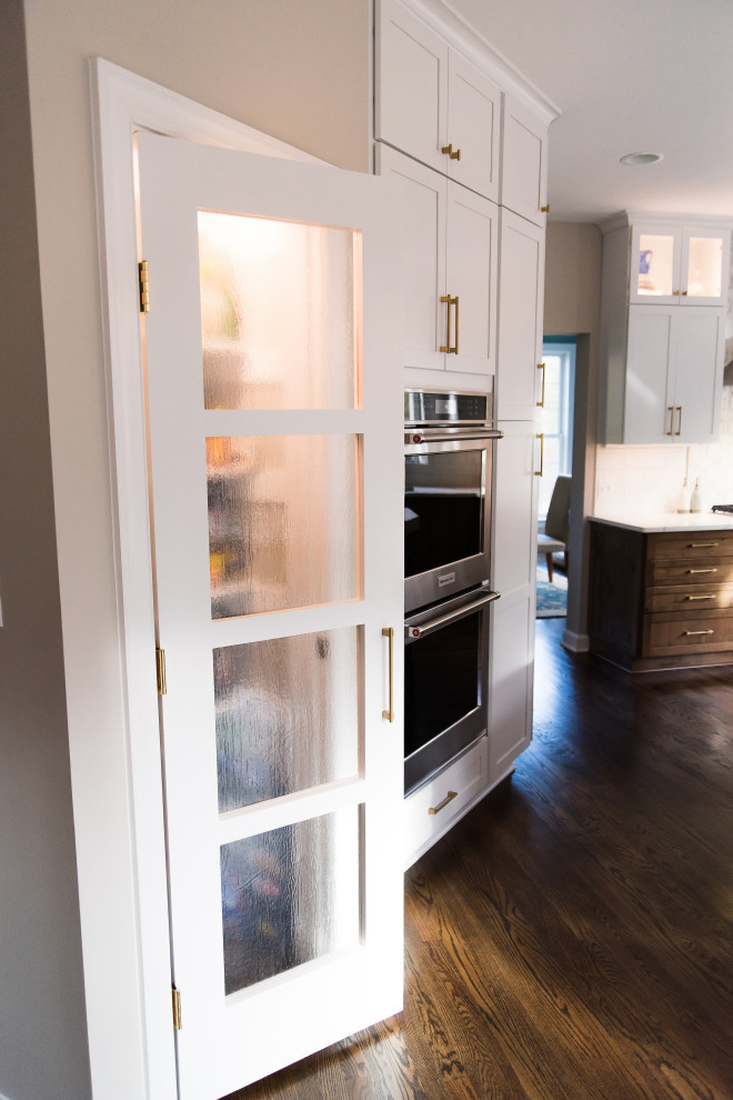 Inspiration for a mid-sized transitional l-shaped dark wood floor and brown floor eat-in kitchen remodel in Baltimore with a single-bowl sink, shaker cabinets, white cabinets, quartz countertops, white backsplash, marble backsplash, stainless steel appliances, an island and white countertops
