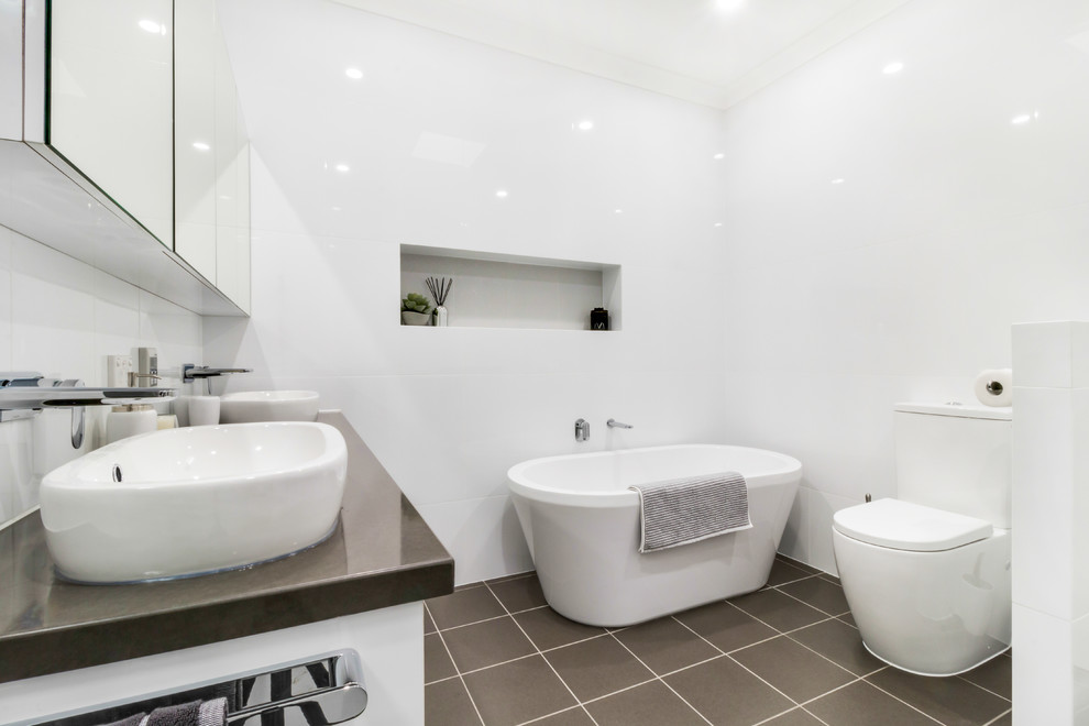 Design ideas for a large modern master wet room bathroom in Adelaide with shaker cabinets, white cabinets, a freestanding tub, a two-piece toilet, white tile, ceramic tile, white walls, ceramic floors, a vessel sink, granite benchtops, brown floor, a hinged shower door and brown benchtops.