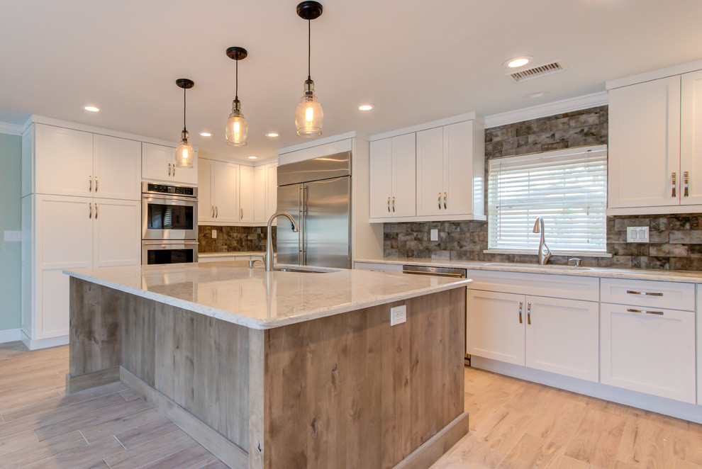 Example of a large transitional u-shaped porcelain tile and brown floor enclosed kitchen design with an undermount sink, shaker cabinets, white cabinets, quartz countertops, brown backsplash, stainless steel appliances, an island and beige countertops