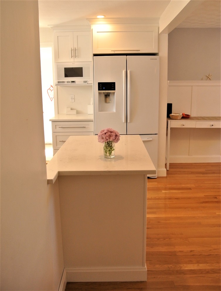Example of a transitional u-shaped medium tone wood floor eat-in kitchen design in Boston with shaker cabinets, an undermount sink, white cabinets, white backsplash, white appliances and a peninsula