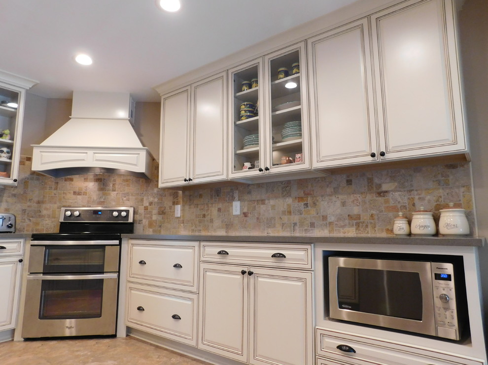 Example of a mid-sized transitional galley vinyl floor enclosed kitchen design with a farmhouse sink, raised-panel cabinets, beige cabinets, solid surface countertops, multicolored backsplash, stone tile backsplash, stainless steel appliances and no island