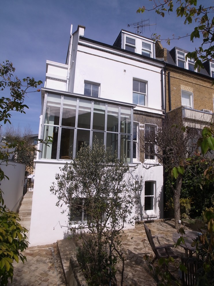 This is an example of a mid-sized contemporary three-storey stucco white exterior in London with a flat roof.
